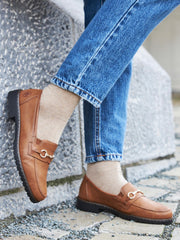Person iført beige sokker, blå jeans og 04396 Rieker Ladies Loafer Cayenne fra Rieker Comfort & Style med metallspennedetaljer, stående på steintrapper utendørs – komfort i høyeste klasse.