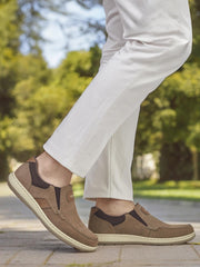 Iført off-white bukser og 07530 Rieker Slip in Loafer Wide Fit Brown fra Rieker Comfort & Style, nyter denne moteriktige mannen hverdagskomfort mens han spaserer utendørs langs en sti omkranset av frodige grønne trær og gress.