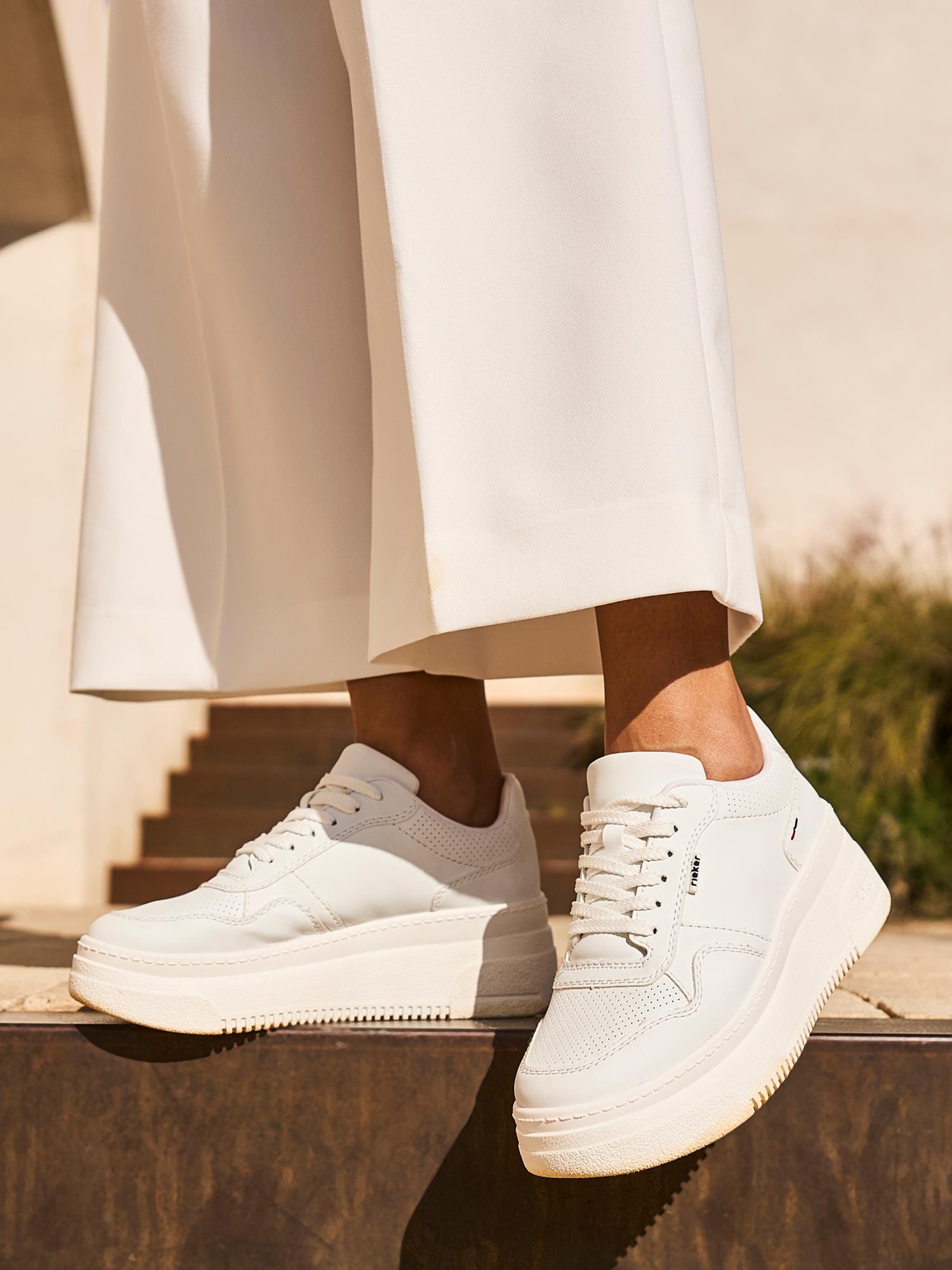 Noen står på et trappetrinn i sollyset iført hvite bukser med vide ben og 03280 Rieker Essential Comfort Sneakers fra Rieker Comfort & Style - perfekte komfortsko som kombinerer Antistress-teknologi med stilfull komfort.