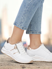 Iført lyseblå jeans og Remontes joggesko 03114 Remonte Draper White Leather står denne personen selvsikkert på en betongflate og utstråler stil og komfort med et uskarpt bylandskap i bakgrunnen.