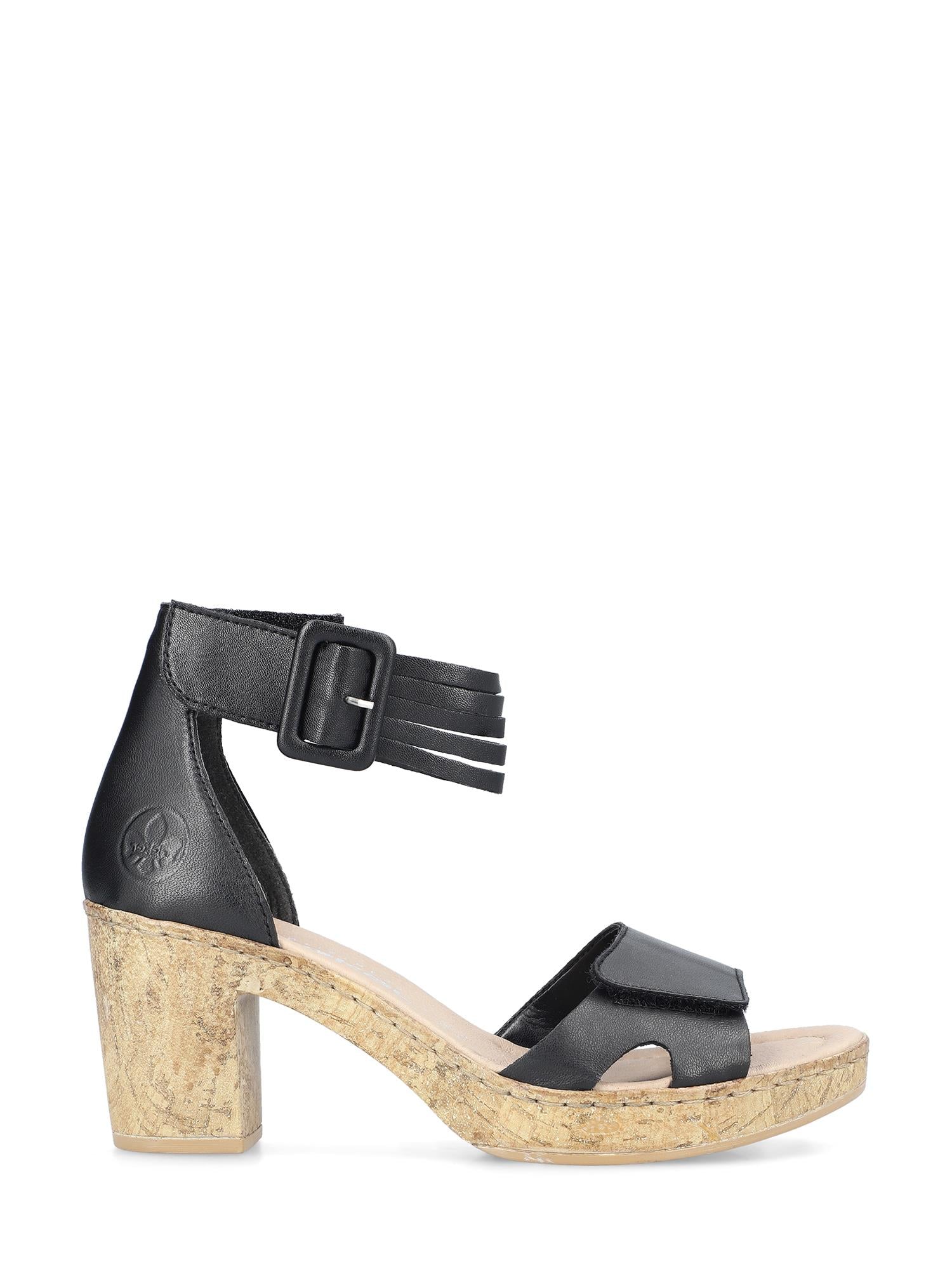 07499 Rieker Malibu Sandal Leather fra Rieker Comfort & Style er en åpen sandal i svart skinn med chunky korkhæl, ankelrem og stor spenne, sett i sideprofil på en hvit bakgrunn - kombinerer komfort og eleganse.