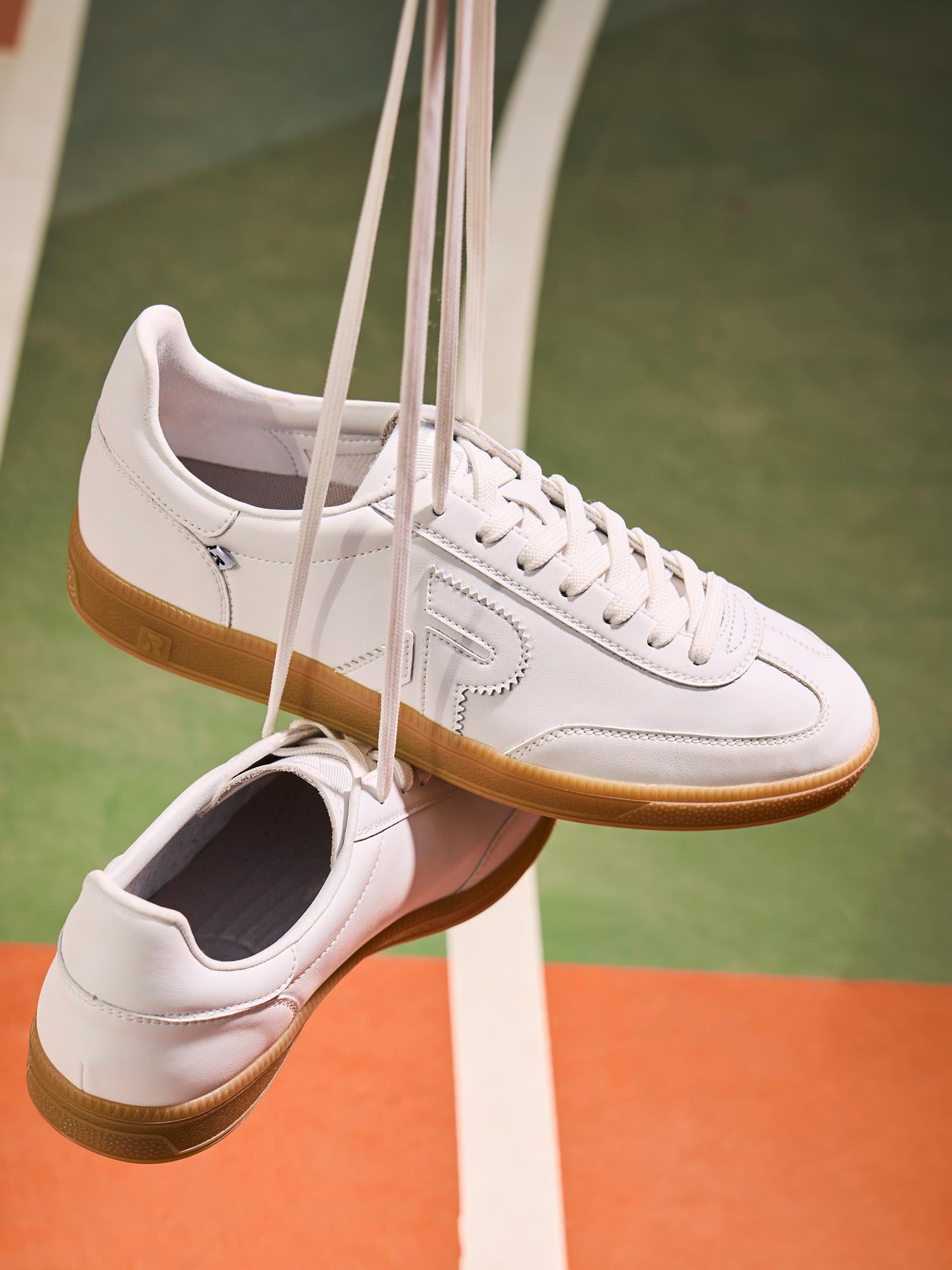 Et par 03336 Rieker San Diego Leather Sneaker Herre Hvit fra Rieker, med solbrune gummisåler, henger i lissene over en sportsbane og forener klassisk design og komfortable trinn over grønne og oransje partier og en dristig hvit linje.