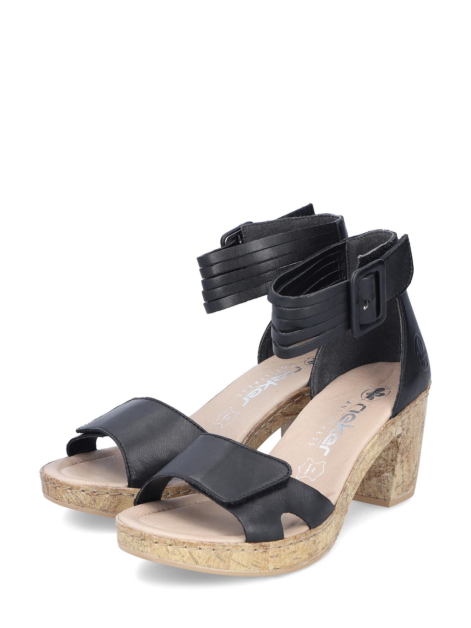 Rieker Comfort & Style 07499 Malibu Sandal Leather har svart skinn, åpne tær, ankelstropper med spenner, blokkhæl med korkstruktur og beige, polstrede innleggssåler for optimal komfort.