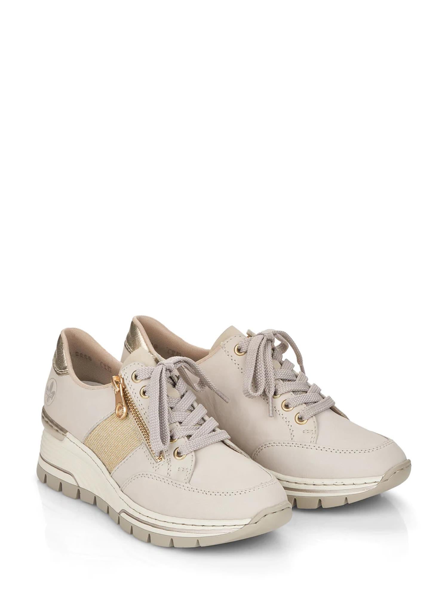 06829 Rieker Golden Beige Sneaker fra Rieker Comfort & Style har et beige snøredesign med gulldetaljer, slank overdel, glidelåser på siden og en tykk hvit og beige kilesåle, vist mot en hvit bakgrunn.